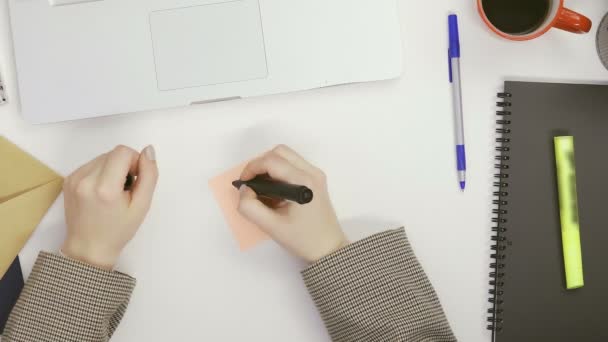 Eine Frau schreibt mit einem Filzstift an einem Tisch in einem hellen Raum Buchstaben auf Memory-Sticker — Stockvideo