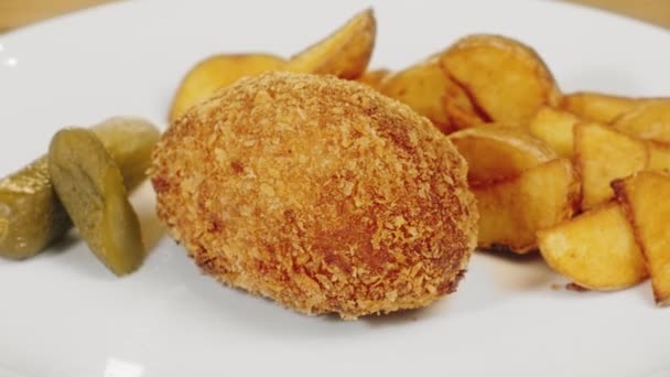 М'ясна котлета, смажена картопля та маринований огірок на білій тарілці крупним планом — стокове відео
