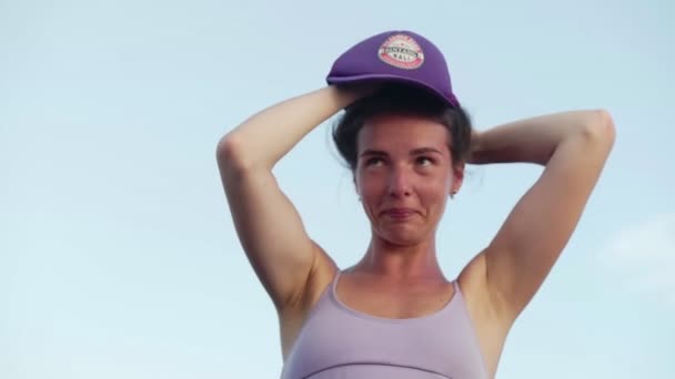 A girl puts on a purple cap against the sky — Stock Video