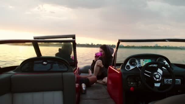 En kille och en tjej sitter i en motorbåt och pratar och tittar på solnedgången. Romantisk atmosfär. — Stockvideo