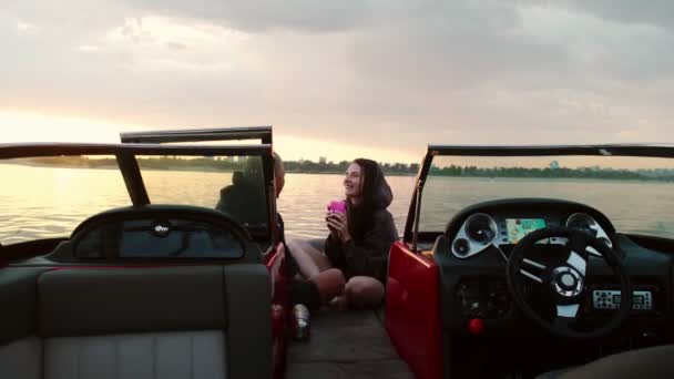 Un homme et une fille sont assis dans un bateau à moteur embrassant et regardant le coucher du soleil. Ambiance romantique. — Video