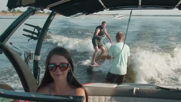 Een vrouw bestuurt een motorboot, en op de achtergrond rijdt een man op een wakeboard, en de man helpt hem — Stockvideo