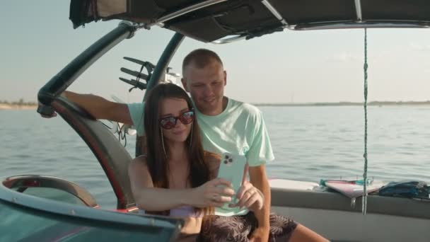 En man och en kvinna sitter i en motorbåt och fotograferar. — Stockvideo