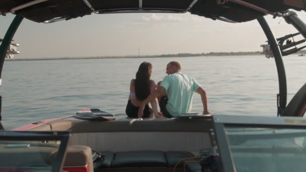Um cara e uma menina estão sentados em um barco a motor, beijando e olhando para a distância. Ambiente romântico. — Vídeo de Stock