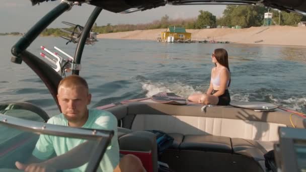 En mand kører en motorbåd, og en kvinde i baggrunden sidder og nyder det behagelige vejr. – Stock-video