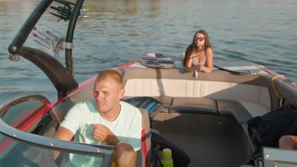 Bir adam motorlu tekne kullanıyor ve arka planda bir kadın yüzüstü uzanıyor ve güzel havanın tadını çıkarıyor. — Stok video