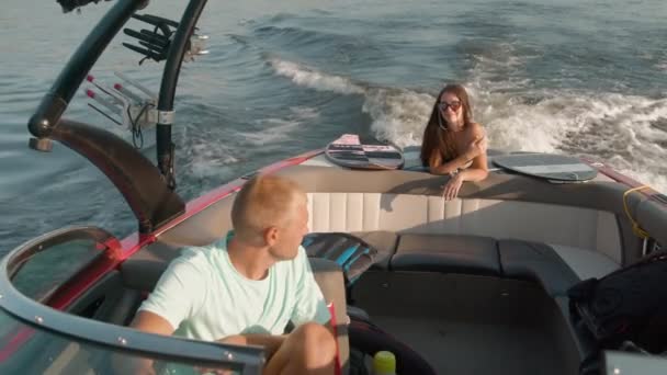 En man kör en motorbåt, och en kvinna i bakgrunden ligger på magen och njuter av det behagliga vädret — Stockvideo
