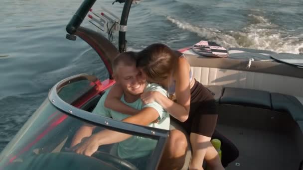 Мужчина водит моторную лодку, а женщина подходит к нему и обнимает его сзади. — стоковое видео