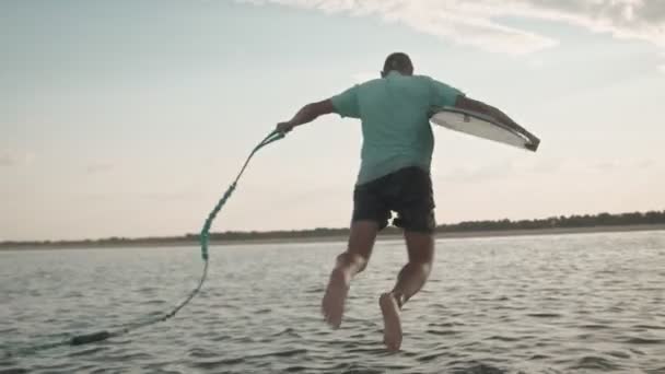 Ένας άντρας με μια σανίδα πηδάει στο νερό. — Αρχείο Βίντεο