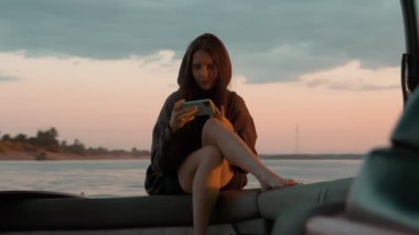 Bir kadın gün batımında motorlu bir teknede telefonda oturuyor.