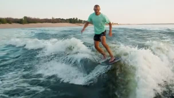 En surfer hopper på et wakeboard. En erfaren wakeboarder sprayer vanndråper i kameraet. – stockvideo