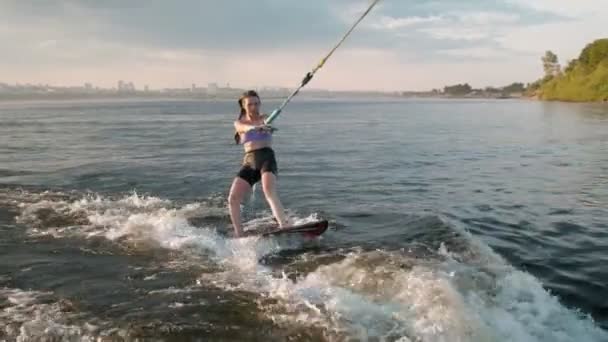 Een vrouwelijke surfer springt op een wakeboard. Een ervaren wakeboarder spat water in de camera. — Stockvideo