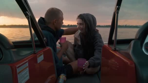 Um cara e uma menina abraçar bonito ao pôr do sol sentado em um barco — Vídeo de Stock