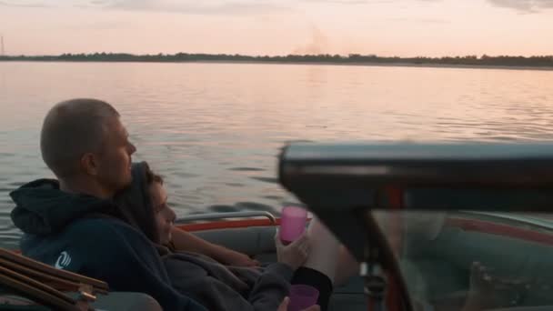 A guy and a girl cuddle cute at sunset sitting in a boat — Stock Video