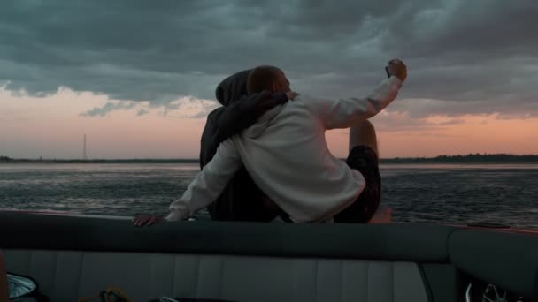 Bir adam ve bir kadın gün batımında bir teknede oturup fotoğraf çekiyorlar. — Stok video