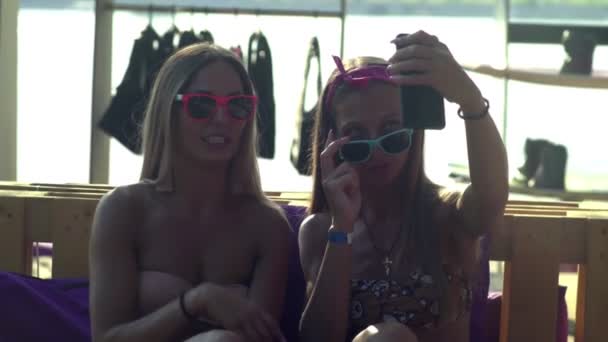 Jonge vrouwen die op zomervakantie gaan, op het strand zitten, een smartphone vasthouden, selfies nemen, een grappige gezichtsuitdrukking tonen — Stockvideo