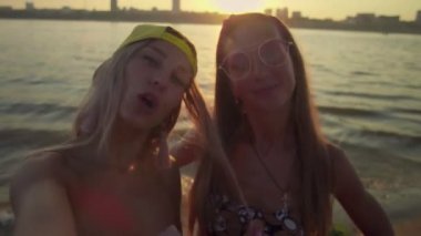 Yaz tatilinde, sahilde gezen, elinde akıllı bir telefonla selfie çeken, komik bir yüz ifadesi gösteren genç kadınlar.