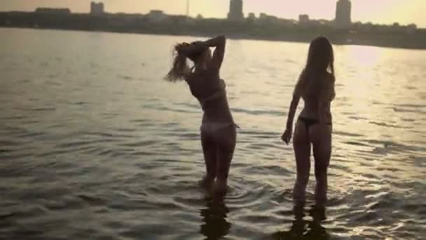 Fiatal gyönyörű lányok örvendeznek a strandon fürdőruhában és nevetnek. Nyár, homokos strand. Naplemente — Stock videók