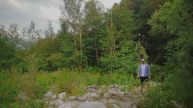 Genç bir adam ormanda yürüyor ve şişeden su içiyor. Açık havada bir adam. Turizm