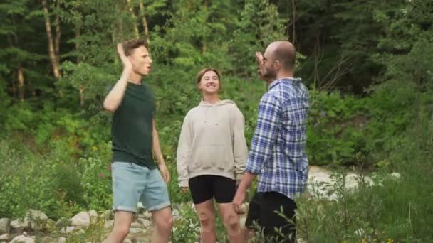 Um grupo de três pessoas dá cinco pontos altos um ao outro enquanto estão em pé em uma floresta cercada por árvores em um dia de verão. Ao ar livre. — Vídeo de Stock