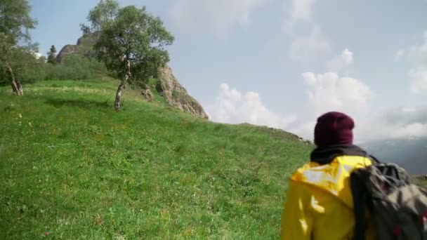 Um turista masculino sobe a montanha com uma capa de chuva amarela, com uma grande mochila nas costas. Turismo. — Vídeo de Stock