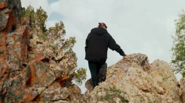 Dağlarda kayaların üzerinde oturan ve uzaklığa bakan bir kızın dikiz görüntüsü. Turizm