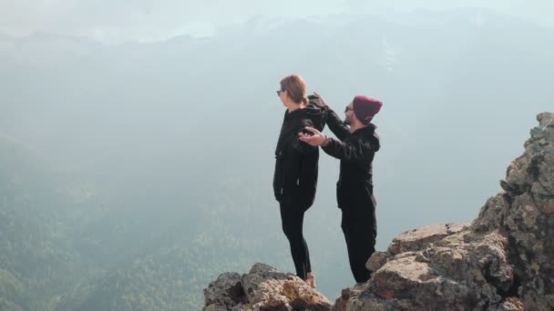Ένα νεαρό ζευγάρι τουριστών στέκεται μαζί σε μια βουνοκορφή, κοιτάζοντας το όμορφο τοπίο. Ο ρομαντισμός στη φύση — Αρχείο Βίντεο