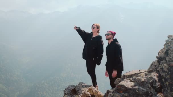 Egy fiatal turista pár együtt áll egy hegycsúcson, és a gyönyörű tájat nézik. Romantika a természetben — Stock videók