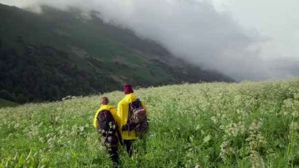 Mladá žena a muž turisté ve žlutých pláštěnkách procházet hornaté oblasti a podívejte se na krásnou přírodu. Cestovní ruch — Stock video