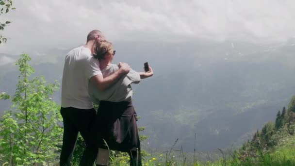 Un giovane uomo e una ragazza sono in piedi in una zona montuosa e scattare selfie sul loro telefono. Viaggio — Video Stock