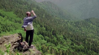 Genç bir adam dağlık bir bölgede bir kayanın üzerinde duruyor ve uzaklığa bakıyor. Seyahat ve turizm