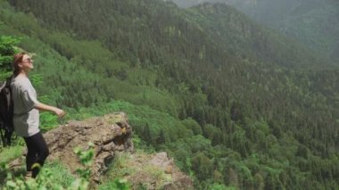 Sırtında sırt çantası olan genç bir kadın dağlık bir bölgedeki bir uçuruma yaklaşıyor ve güzel manzaralara bakıyor. Seyahat ve turizm