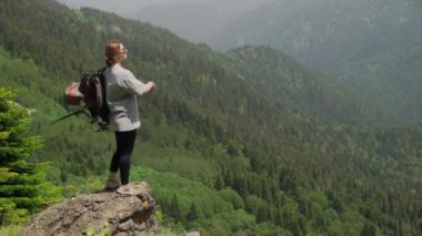 Genç ve mutlu bir turist dağlık bir bölgede uçurumun tepesinde duruyor ve güzel manzaranın tadını çıkarıyor. Turizm ve seyahat
