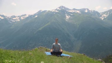 Genç bir kadın dağların tepesinde yoga yapıyor. Spor turizmi