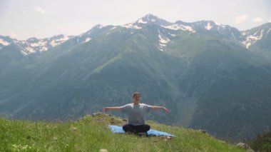 Genç bir kadın dağların tepesinde yoga yapıyor. Spor turizmi