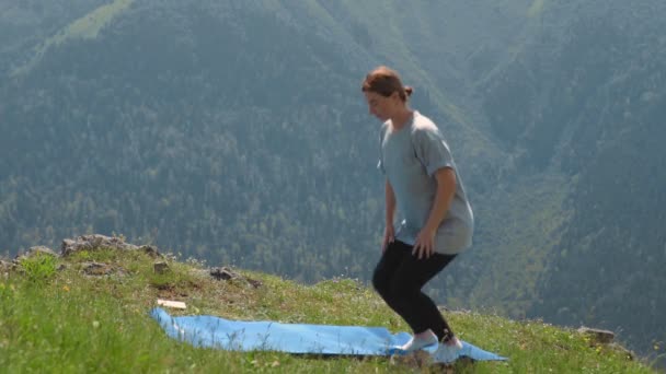 Genç bir kadın dağların tepesinde yoga yapıyor. Spor turizmi — Stok video