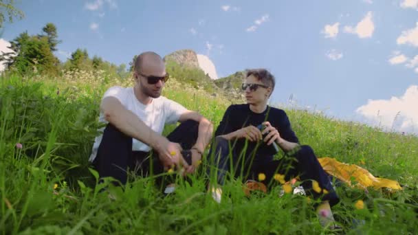 Deux jeunes hommes à lunettes noires sont assis sur une pente, discutant de la vie dans les hauts plateaux. L'un soutient l'autre. Tourisme et voyages — Video