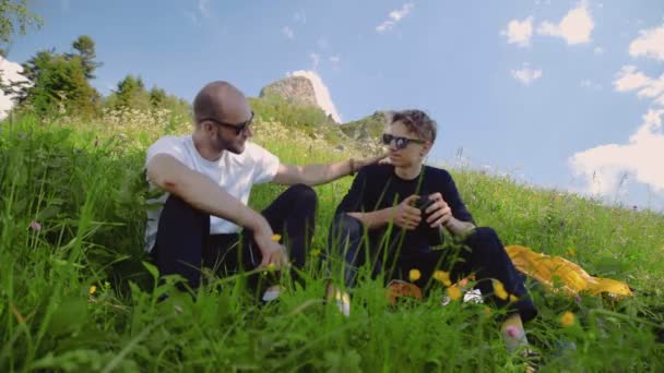 Deux jeunes hommes à lunettes noires sont assis sur une pente, discutant de la vie dans les hauts plateaux. L'un soutient l'autre. Tourisme et voyages — Video