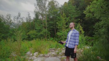 Genç bir adam ormanda duruyor ve şişeden su içiyor. Açık havada bir adam. Turizm