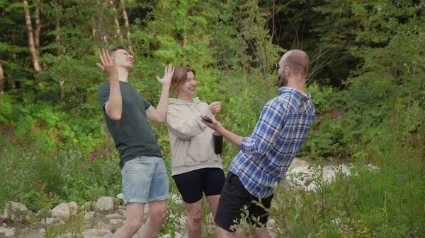 Eine Gruppe von drei Menschen redet und lacht, während sie an einem Sommertag in einem Wald steht, der von Bäumen umgeben ist. Draußen — Stockfoto