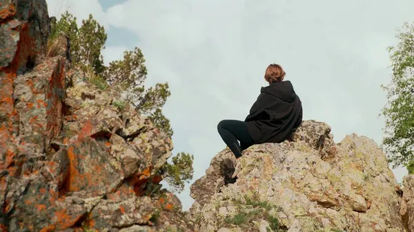 少女は山の中の岩の上に座って、距離を見ての背面ビュー。観光 — ストック写真