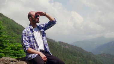 Güneş gözlüklü genç bir adam, bir kayanın üzerinde oturuyor ve hayatın tadını çıkarıyor. Turizm ve seyahat