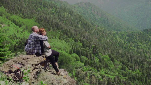 En ung man och en flicka sitter på en klippa i ett bergigt område och tittar på vackra landskap. Turism — Stockfoto