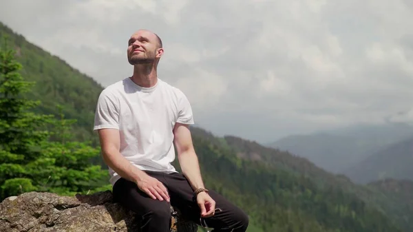 Um jovem está sentado em uma rocha e desfrutando a vida em uma área montanhosa. Turismo e viagens — Fotografia de Stock