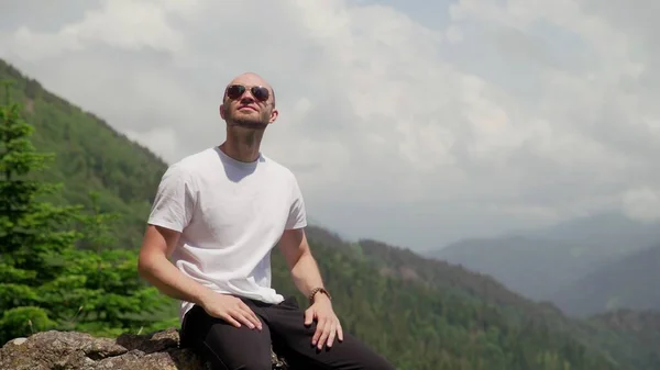 Um jovem de óculos de sol, sentado em uma rocha e desfrutando da vida. Turismo e viagens — Fotografia de Stock