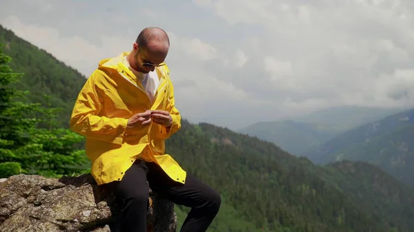 暗い眼鏡の若い男は、岩の上に座って黄色のレインコートをボタン。旅行・観光 — ストック写真