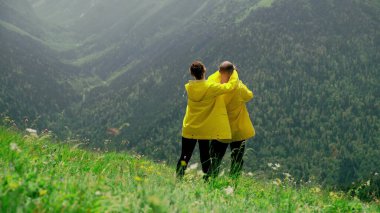 Sarı yağmurluk giymiş genç bir kadın yamaçtan bir adamın yanına gider ve elleriyle gözlerini kapatır. Genç bir çift birbirlerine sevinir. Seyahat ve turizm