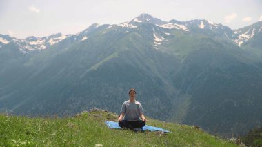 Genç bir kadın dağların tepesinde yoga yapıyor. Spor turizmi