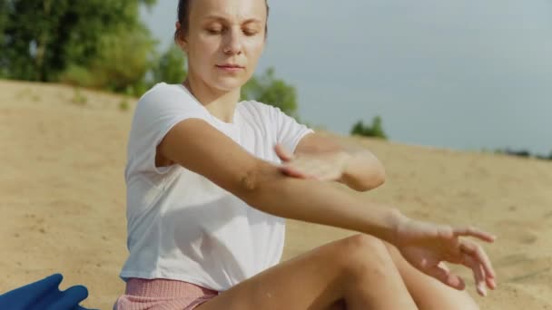 Una giovane donna è seduta sulla spiaggia e si spalma di crema solare. Riposo — Video Stock