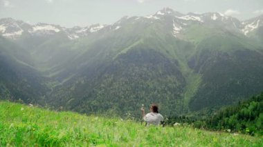 Genç bir kadın bir yamaçta oturuyor ve dağlık alanların muhteşem manzarasının tadını çıkarıyor. Turizm ve seyahat